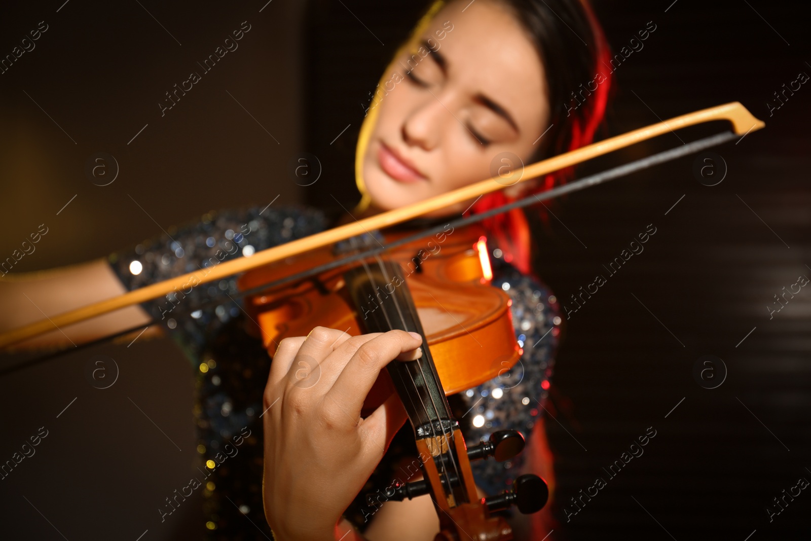 Photo of Beautiful young woman playing violin in dark room, focus on hand