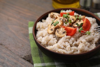 Photo of Delicious barley porridge with mushrooms, tomatoes and microgreens in bowl on wooden table, closeup