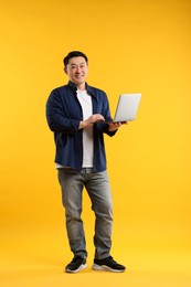 Full length portrait of happy man with laptop on yellow background