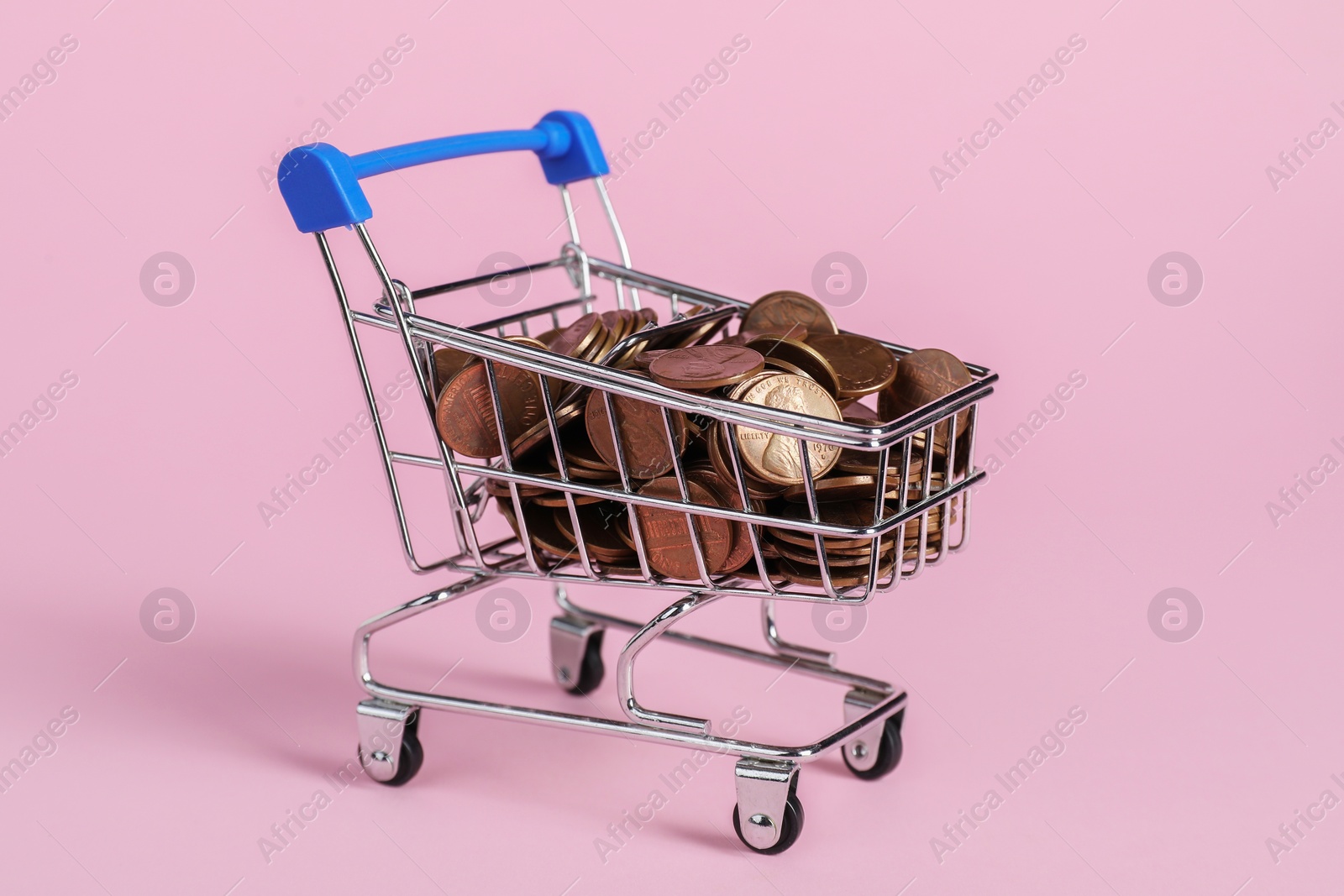 Photo of Small metal shopping cart with coins on pink background