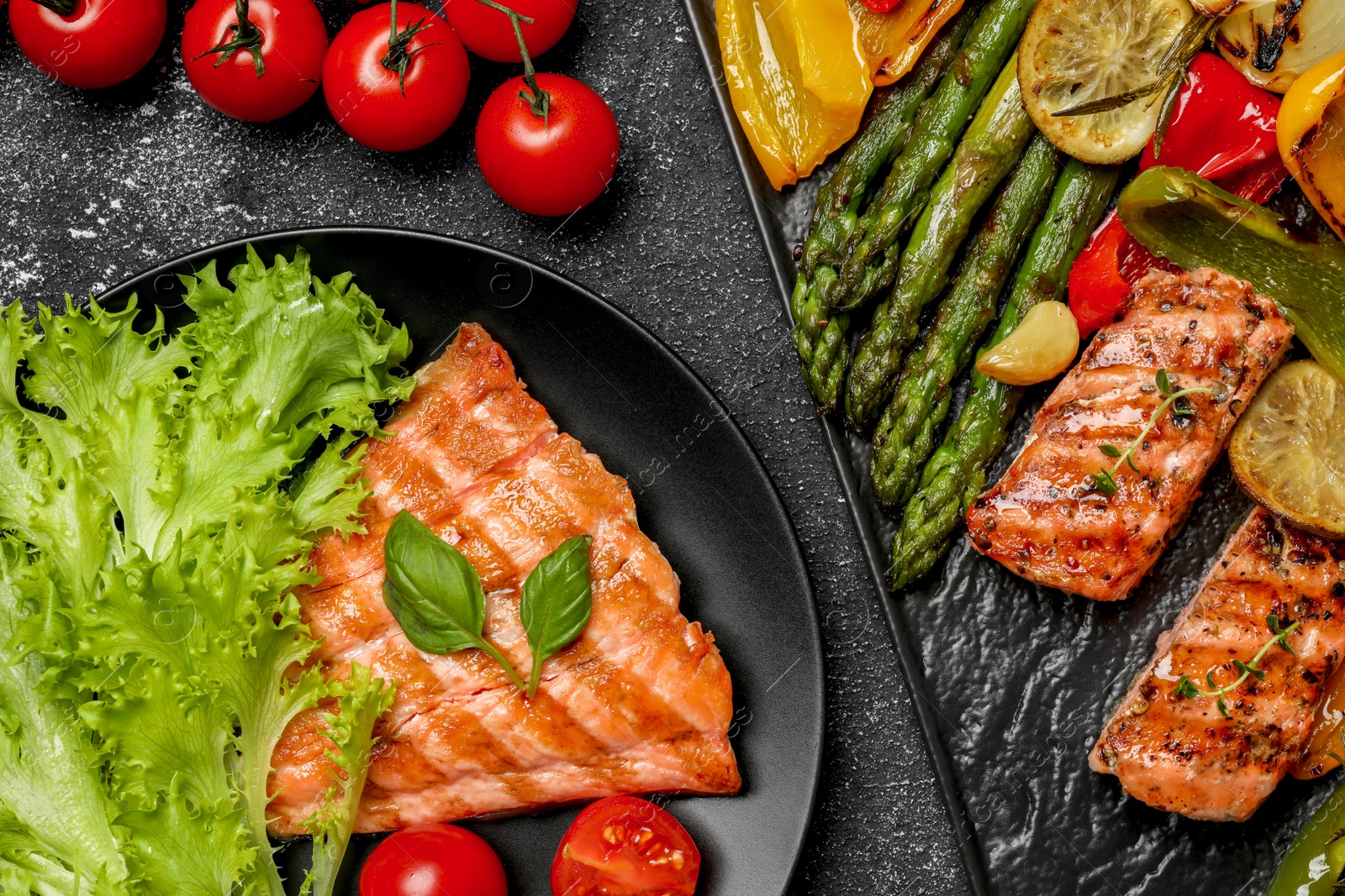 Photo of Tasty cooked salmon with fresh and grilled vegetables on black table, flat lay