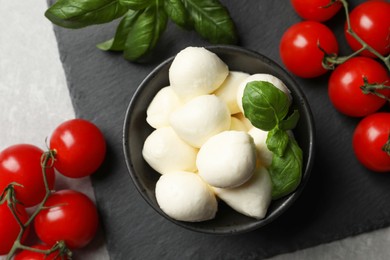 Photo of Delicious mozzarella balls, basil and tomatoes on light gray table, flat lay