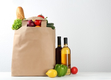 Photo of Shopping paper bag with different groceries on table against white background. Space for text