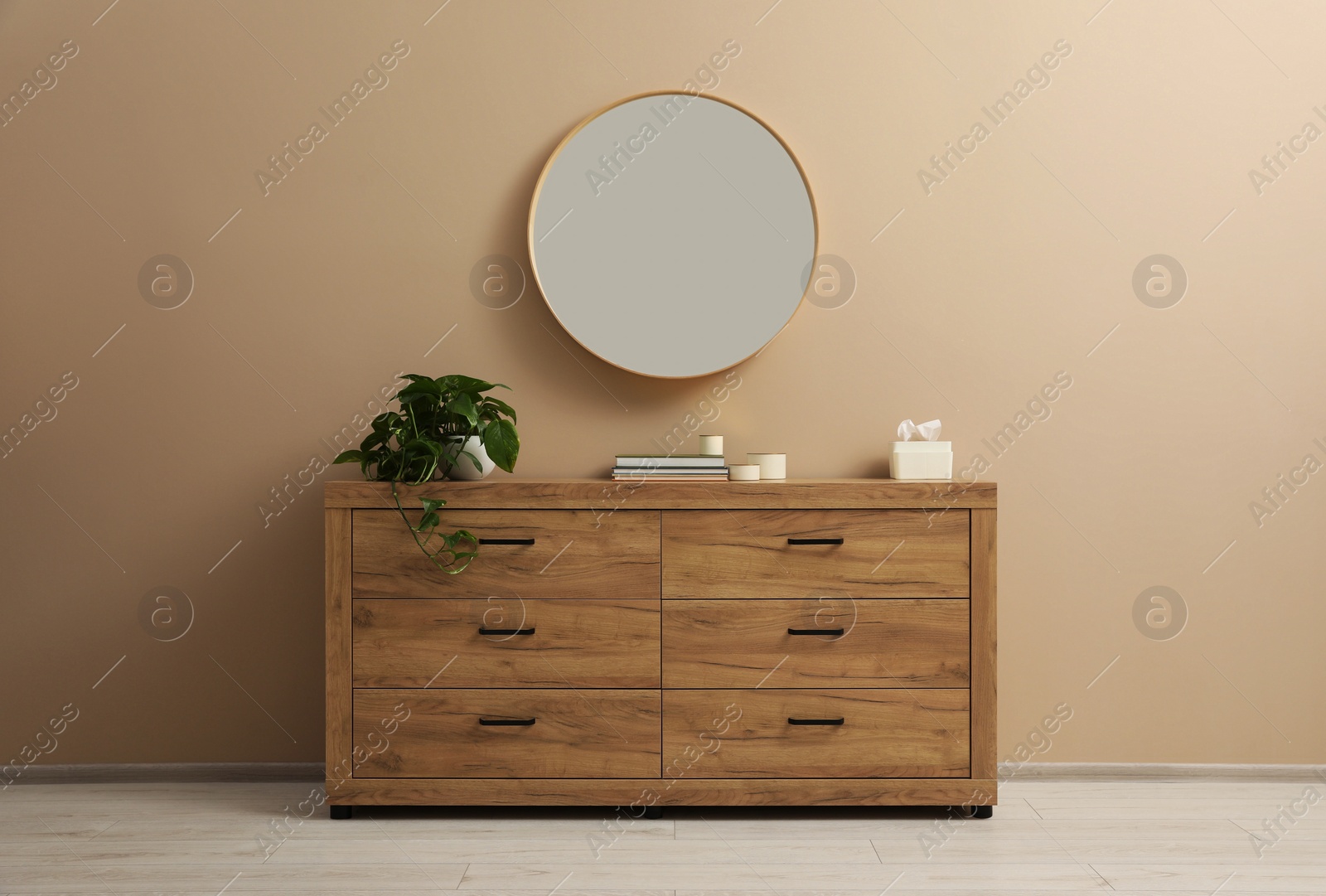 Photo of Wooden stylish chest of drawers near light brown wall with round mirror