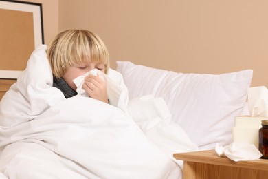 Photo of Boy blowing nose in tissue in bed at home. Cold symptoms