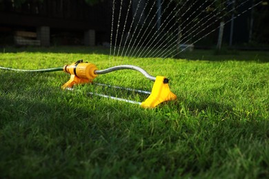 Photo of Automatic sprinkler watering green grass on lawn outdoors. Irrigation system