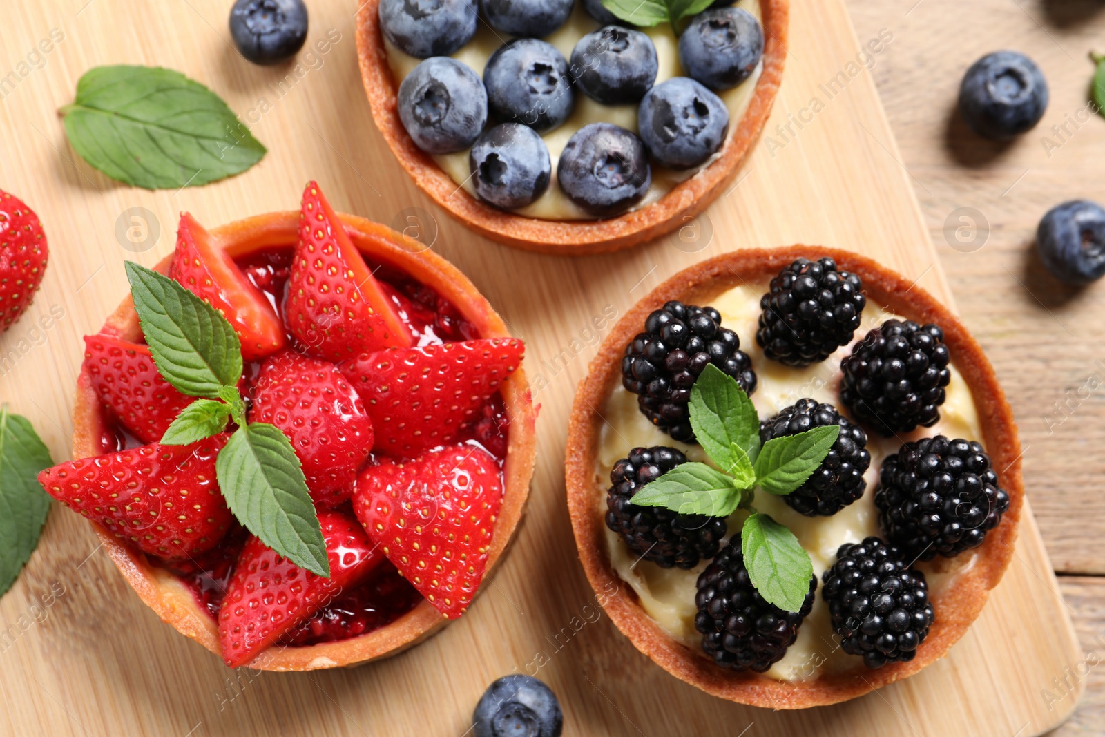 Photo of Tartlets with different fresh berries on wooden table, flat lay. Delicious dessert