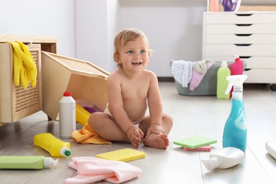 Photo of Cute baby surrounded by cleaning supplies at home. Dangerous situation