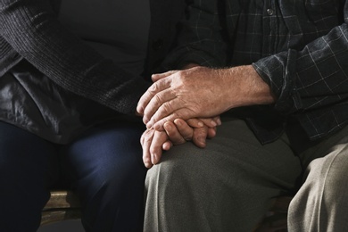 Poor elderly couple holding hands together, closeup