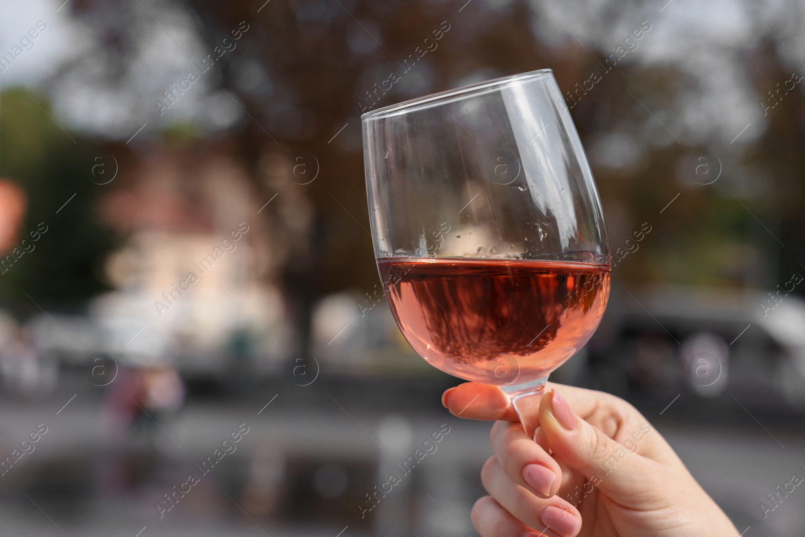 Photo of Woman holding glass of rose wine outdoors, closeup. Space for text