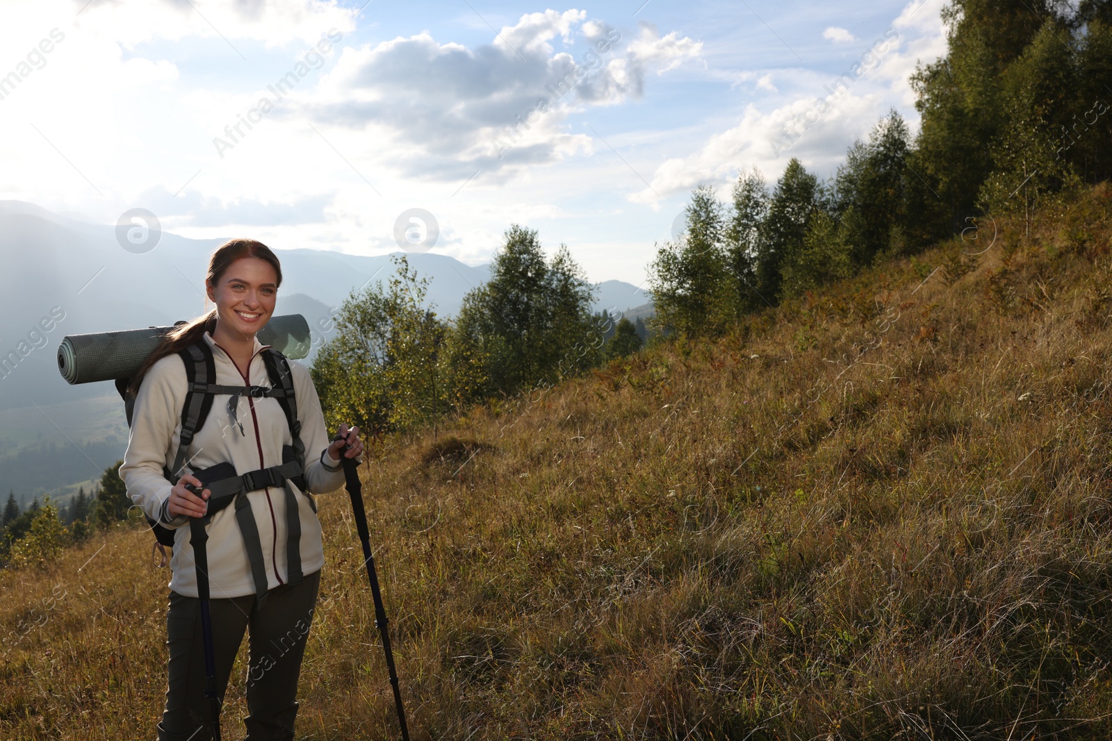 Photo of Tourist with backpack and trekking poles hiking through mountains, space for text