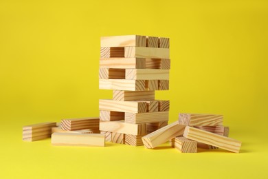 Photo of Jenga tower and wooden blocks on yellow background
