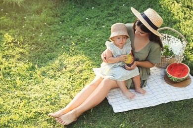 Photo of Mother with her baby daughter having picnic on green grass outdoors, space for text