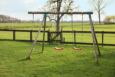 Wooden swings near fence outdoors on spring day