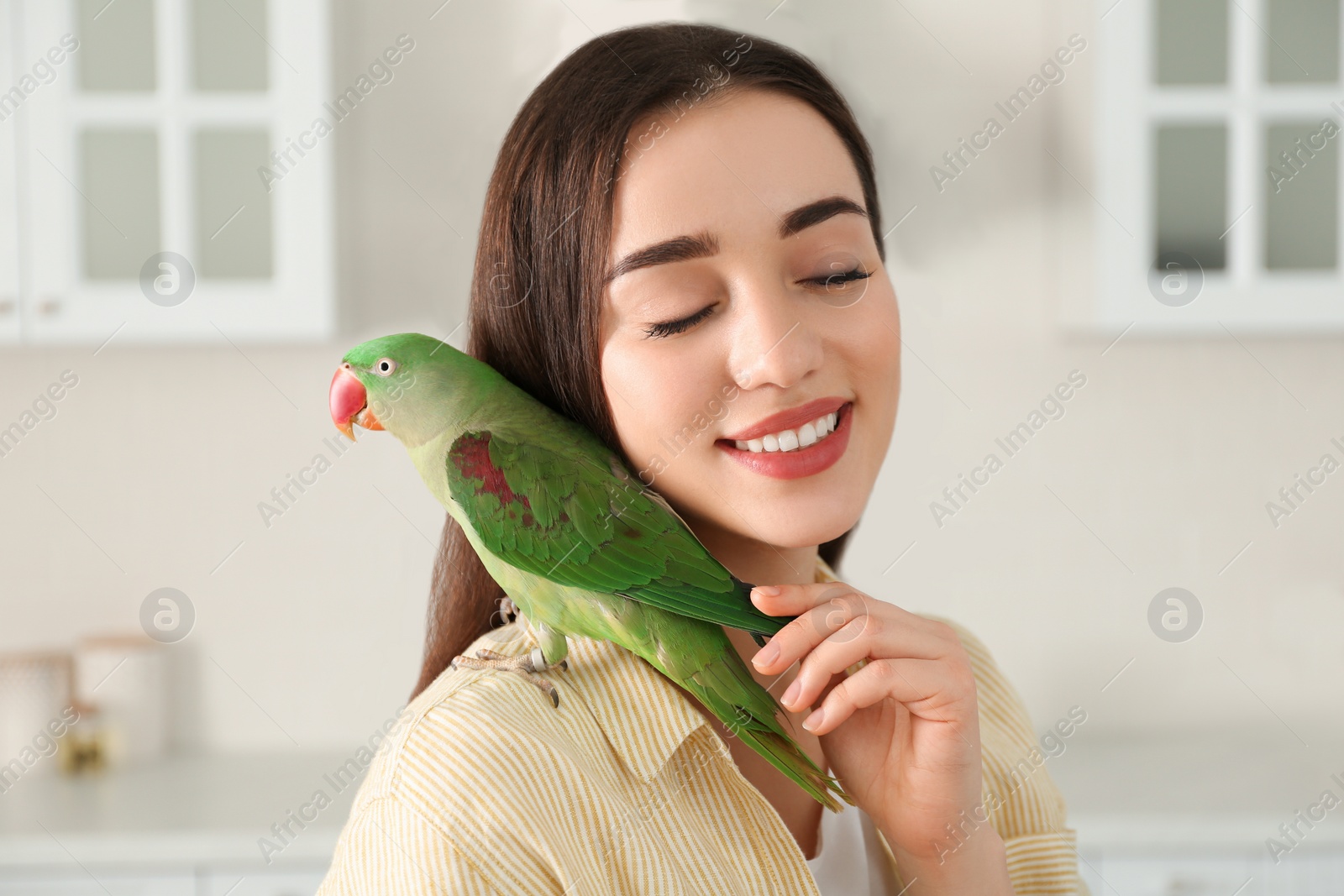 Photo of Young woman with Alexandrine parakeet indoors. Cute pet