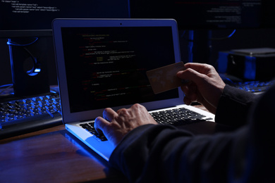 Photo of Hacker with computers and credit card in dark room, closeup. Cyber crime