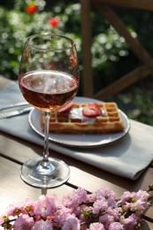 Photo of Delicious Belgian waffle with fresh strawberries and wine served on table in spring garden