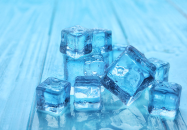 Photo of Crystal clear ice cubes with water drops on blue wooden table