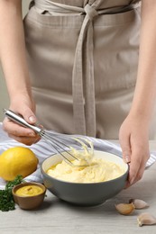Photo of Woman making homemade mayonnaise in ceramic bowl at wooden table, closeup