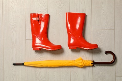 Photo of Flat lay composition with umbrella and rubber boots on wooden background