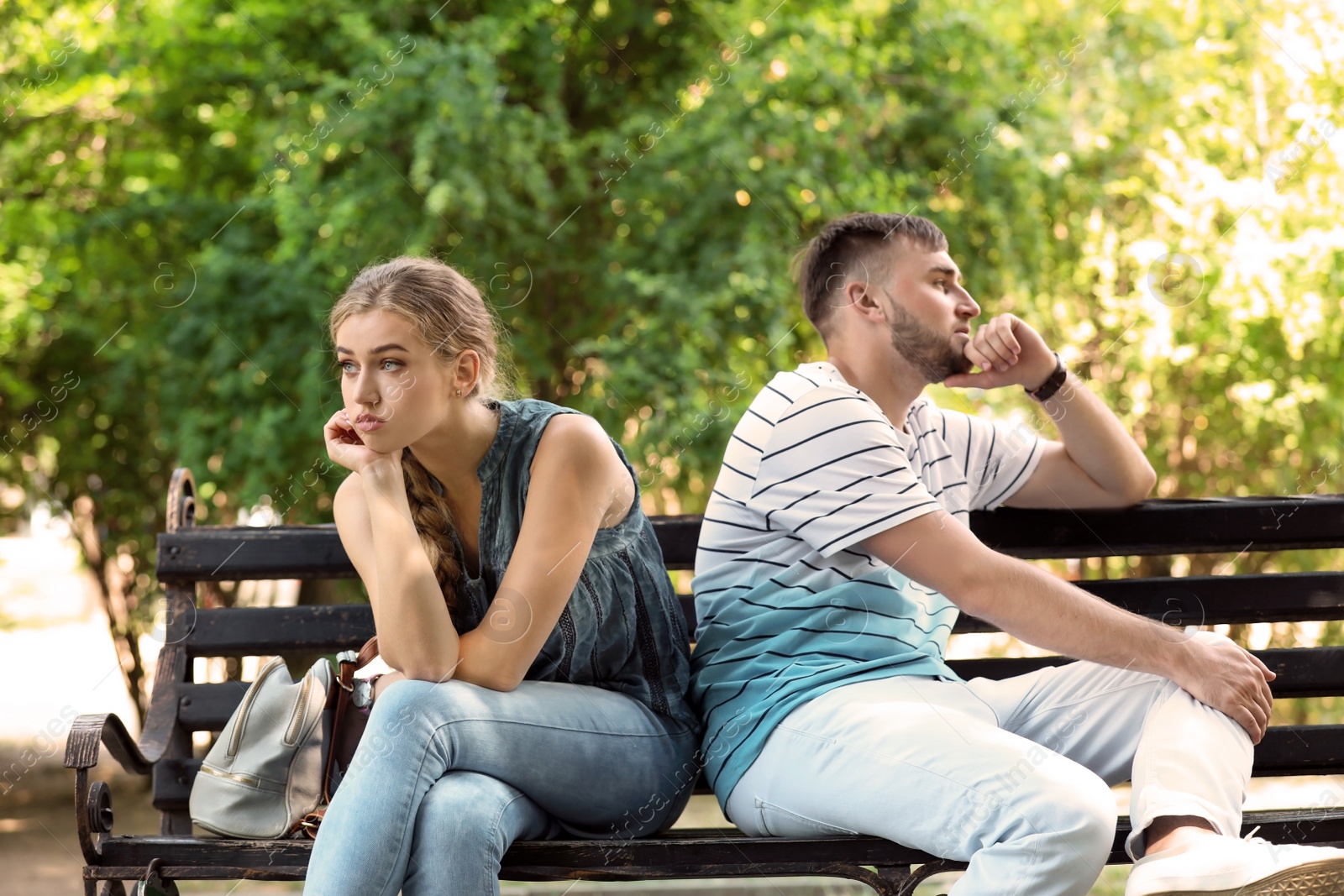 Photo of Young couple arguing while sitting on bench in park. Problems in relationship