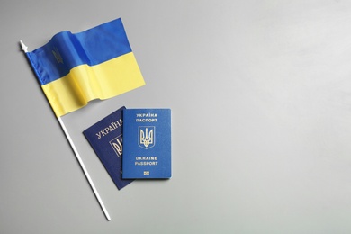 Photo of Ukrainian passports and national flag on grey background, top view with space for text. International relationships