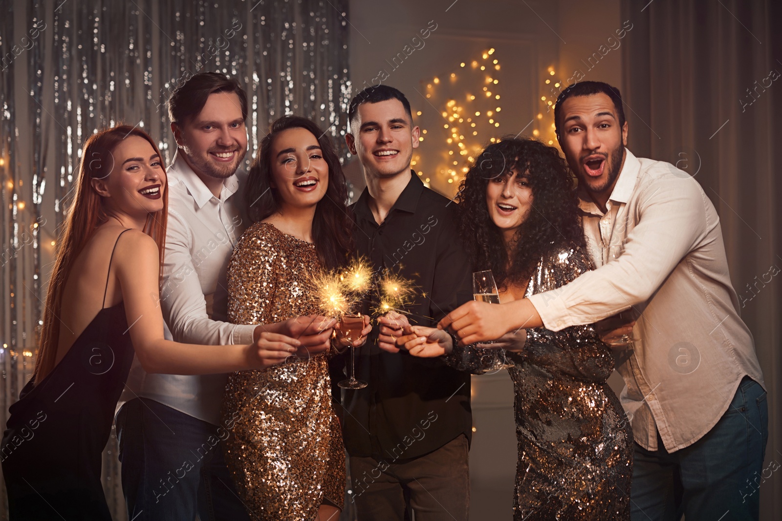 Photo of Happy friends with glasses of wine and sparklers celebrating birthday indoors