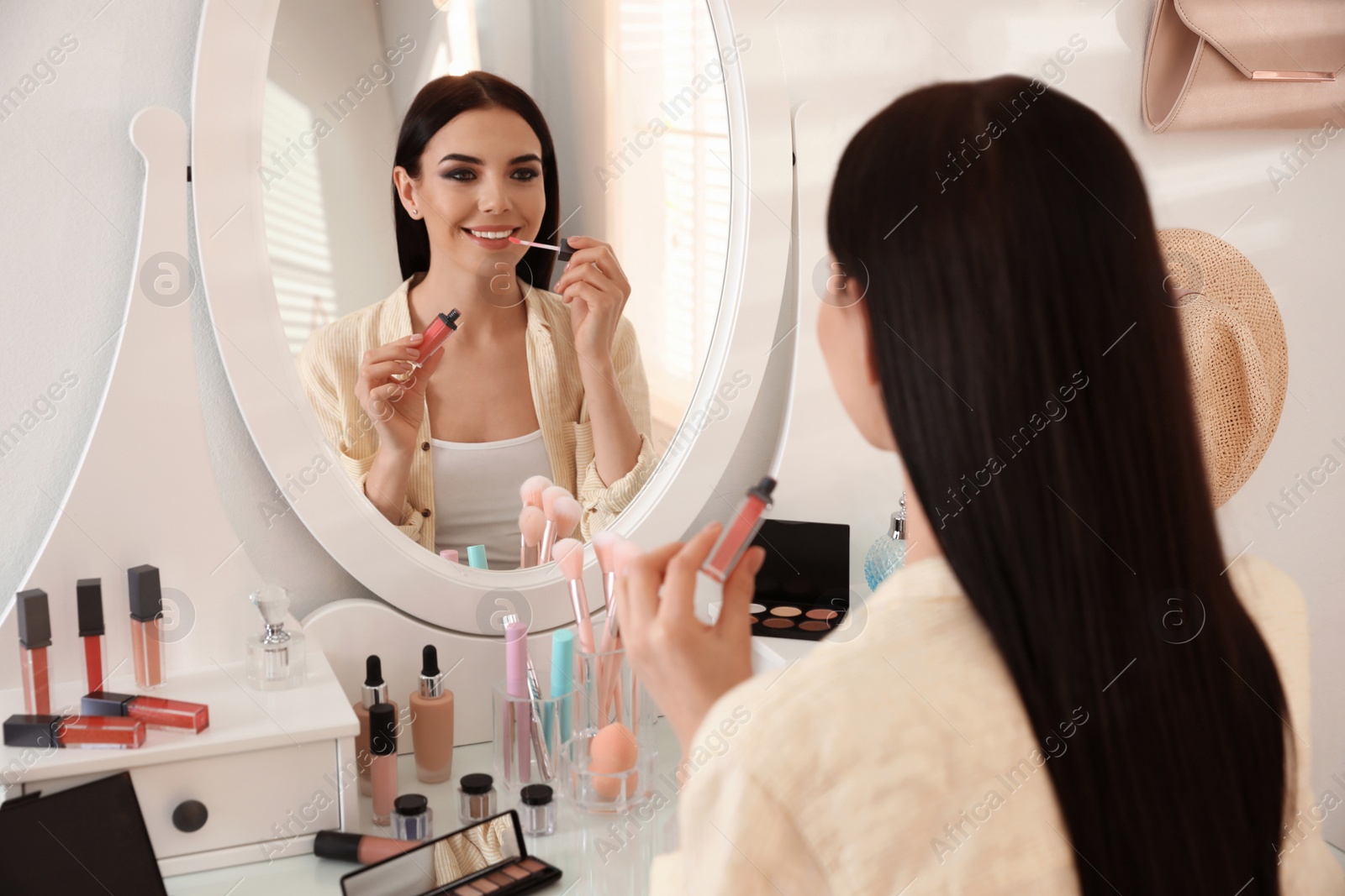 Photo of Beautiful young woman applying makeup near mirror indoors