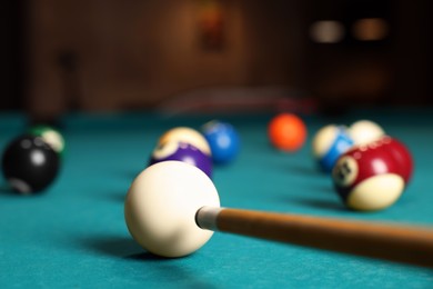 Many colorful billiard balls and cue on green table indoors, closeup