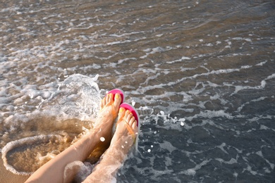 Photo of Closeup of woman with flip flops on sand near sea, space for text. Beach accessories