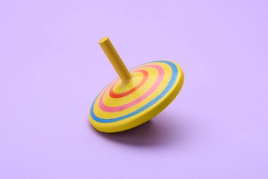 Photo of One bright spinning top on lilac background. Toy whirligig