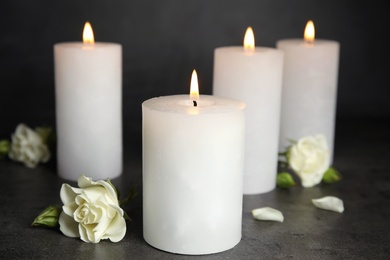 Photo of Burning candles and flowers on dark grey table