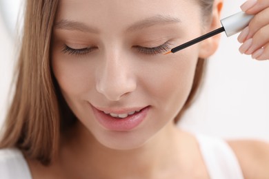 Photo of Beautiful woman applying serum onto eyelashes indoors, closeup