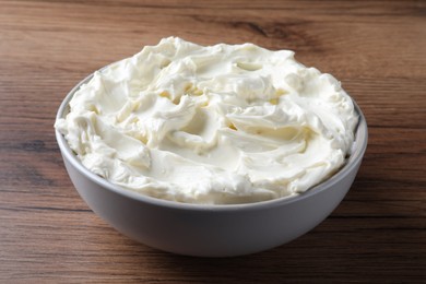 Photo of Bowl of tasty cream cheese on wooden table