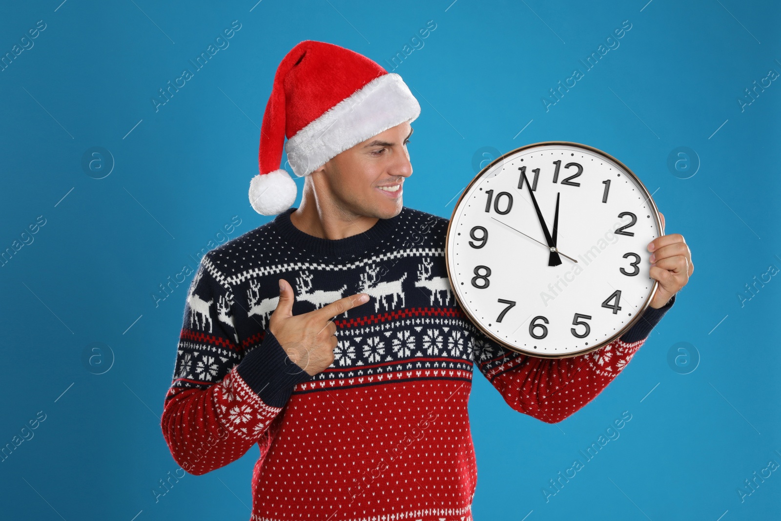 Photo of Man in Santa hat with clock on blue background. New Year countdown