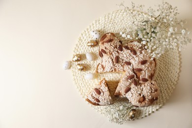 Photo of Wicker mat with delicious Italian Easter dove cake (traditional Colomba di Pasqua), painted eggs and beautiful gypsophila on beige table, flat lay. Space for text