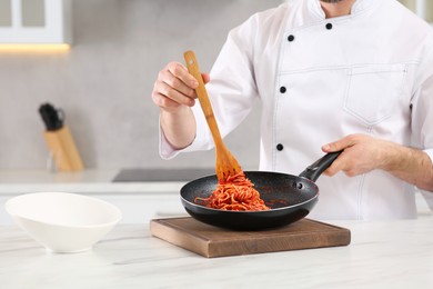 Photo of Professional chef with delicious spaghetti at marble table in kitchen, closeup