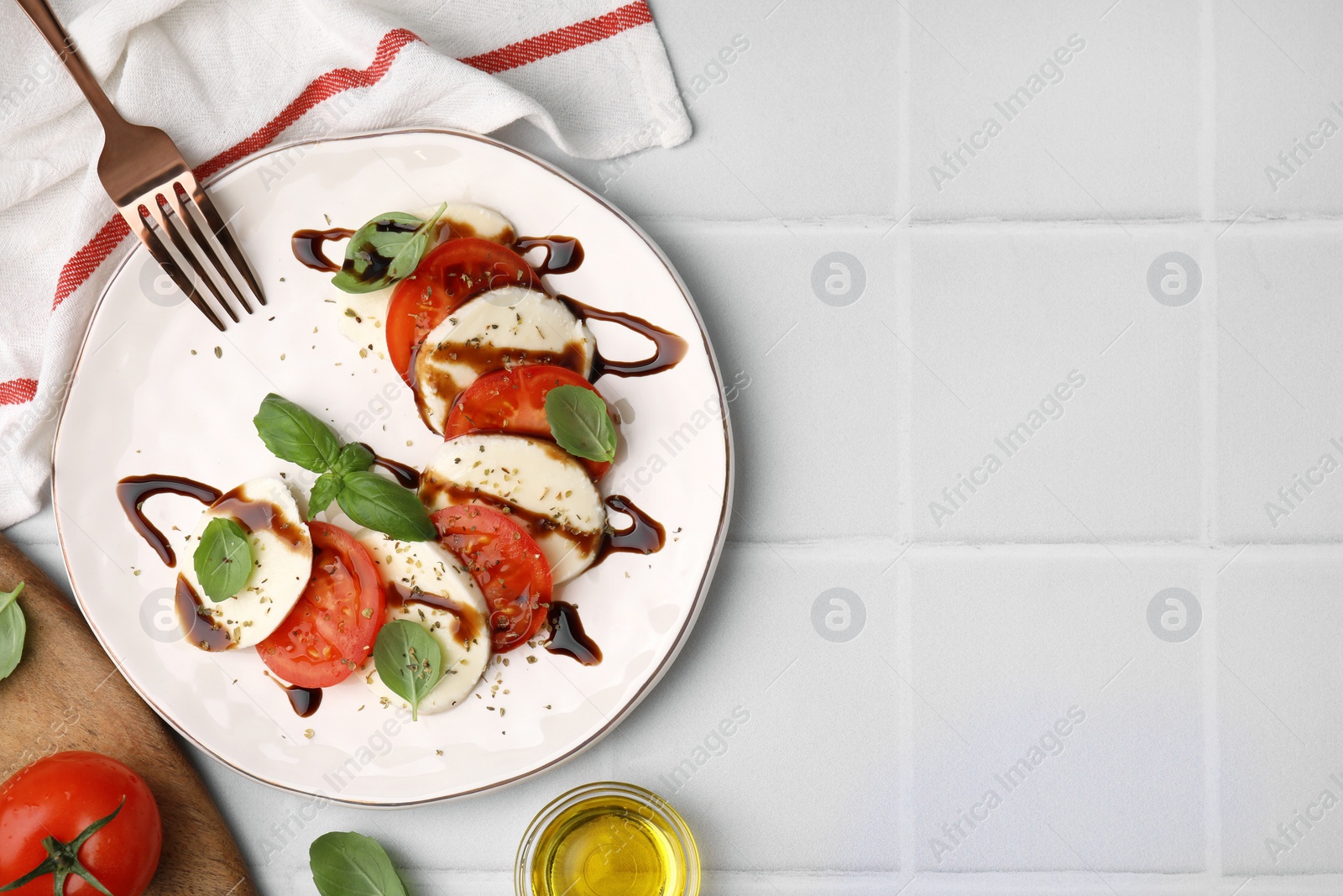 Photo of Delicious Caprese salad with balsamic vinegar served on white tiled table, flat lay. Space for text