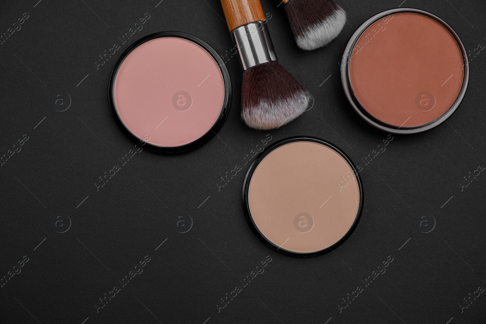 Photo of Different face powders and makeup brushes on black background, flat lay. Space for text