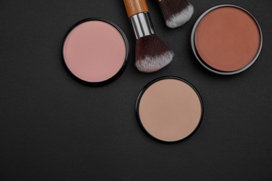 Photo of Different face powders and makeup brushes on black background, flat lay. Space for text