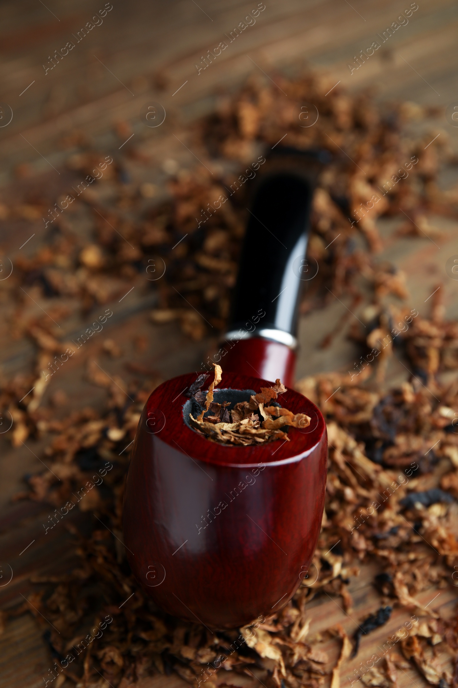 Photo of Smoking pipe and dry tobacco on wooden table, closeup