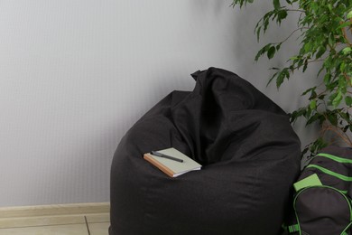 Photo of Black bean bag chair, houseplant and backpack near light grey wall in room. Space for text