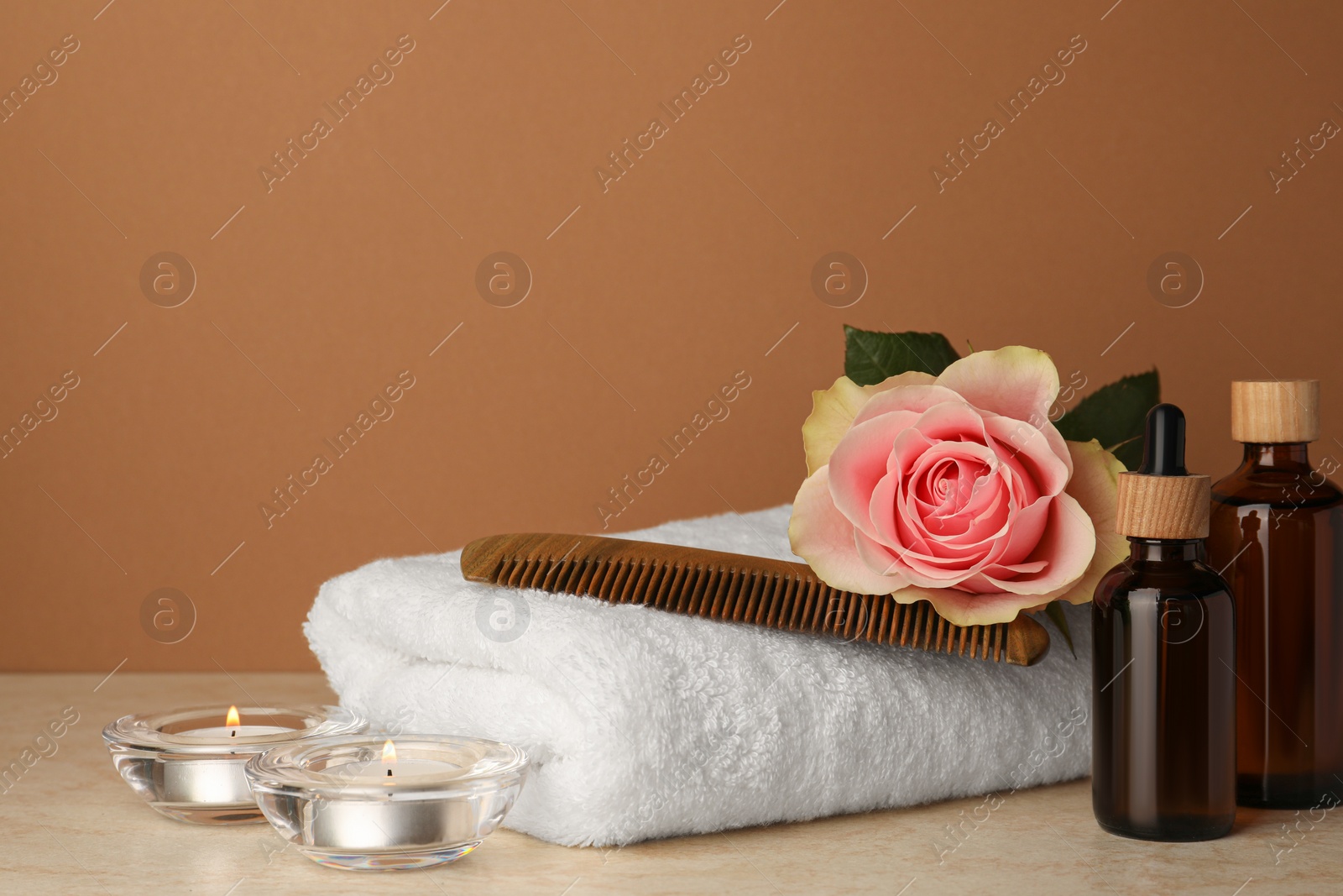 Photo of Composition with different spa products, beautiful flower and burning candles on beige table against brown background. Space for text