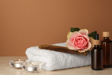 Photo of Composition with different spa products, beautiful flower and burning candles on beige table against brown background. Space for text