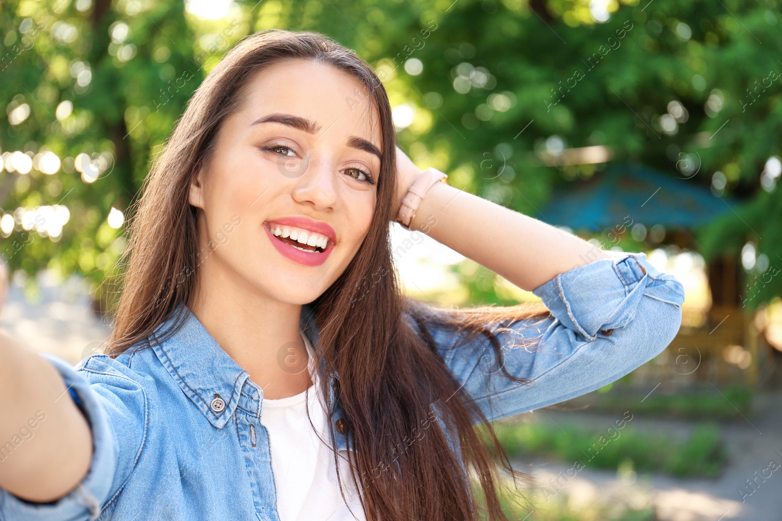 Photo of Young woman taking selfie outdoors on sunny day