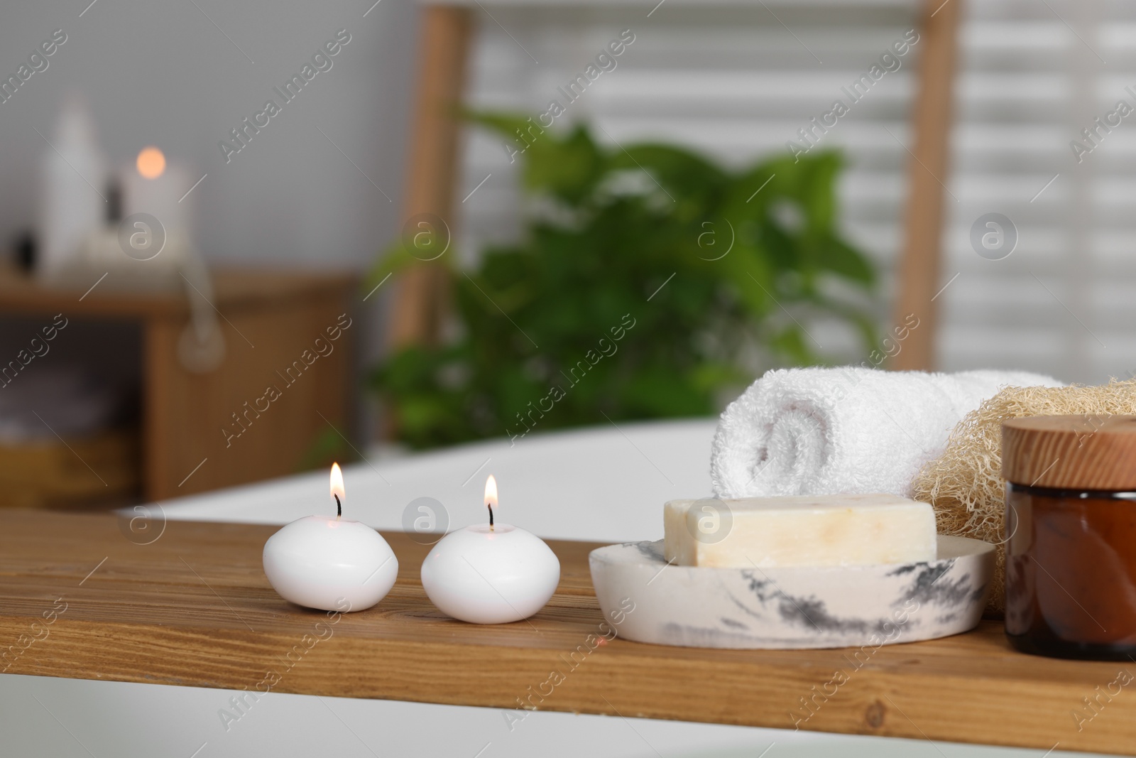 Photo of Wooden board with spa products and burning candles on bath tub in bathroom, space for text