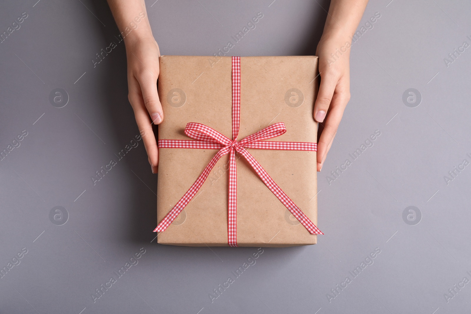 Photo of Woman holding gift box on grey background, top view