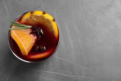 Glass with mulled wine on grey table, top view. Space for text