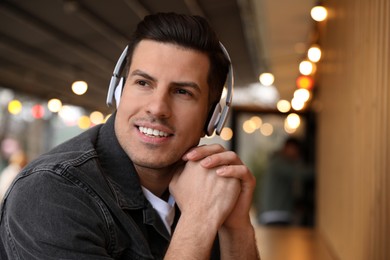 Handsome man with headphones listening to music in outdoor cafe, space for text