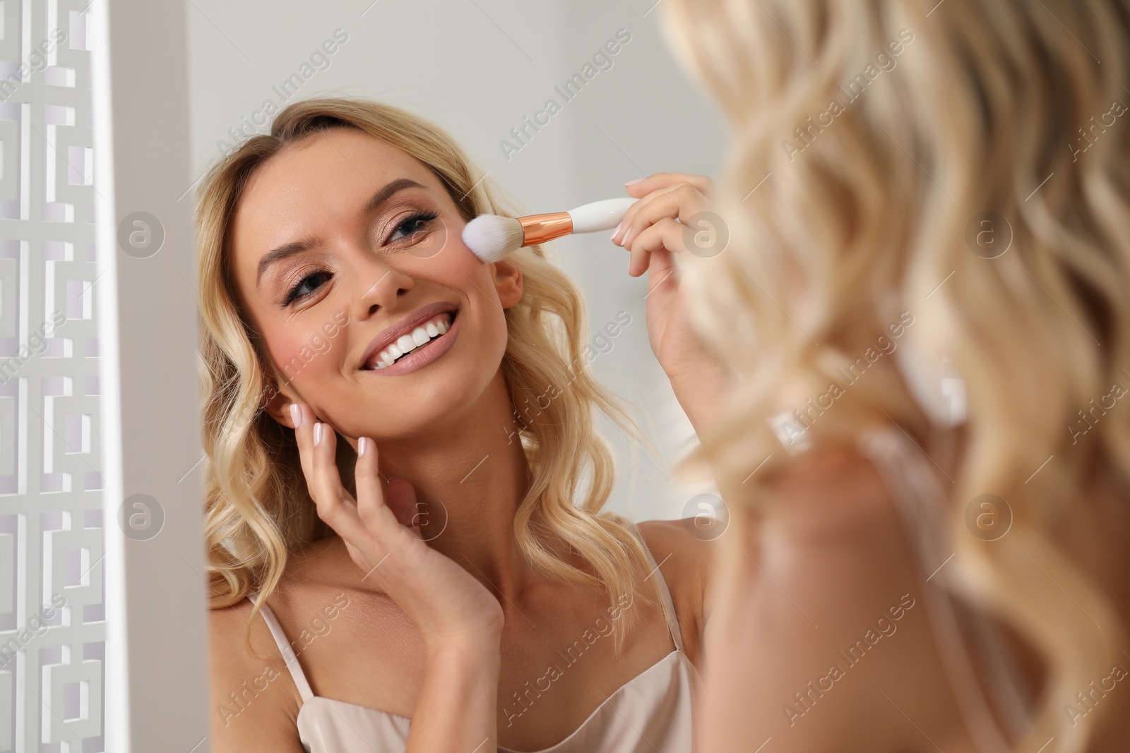 Photo of Beautiful makeup. Smiling woman with brush in front of mirror indoors